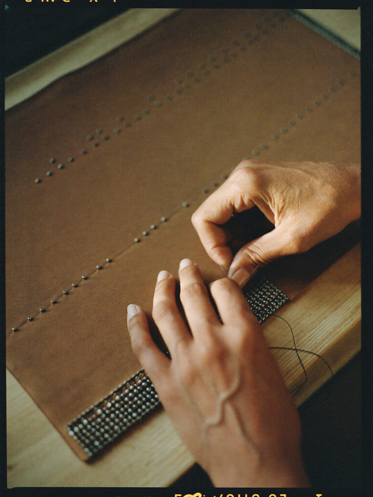An artisan's hands sewing glass beads onto cinnamon silk, needle mid-stitch